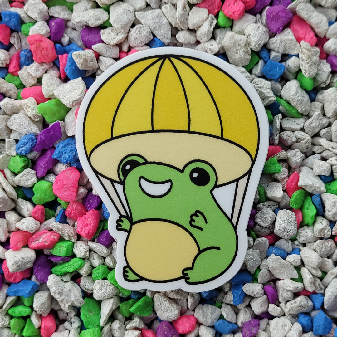 A vinyl sticker featuring a smiling frog parachuting.