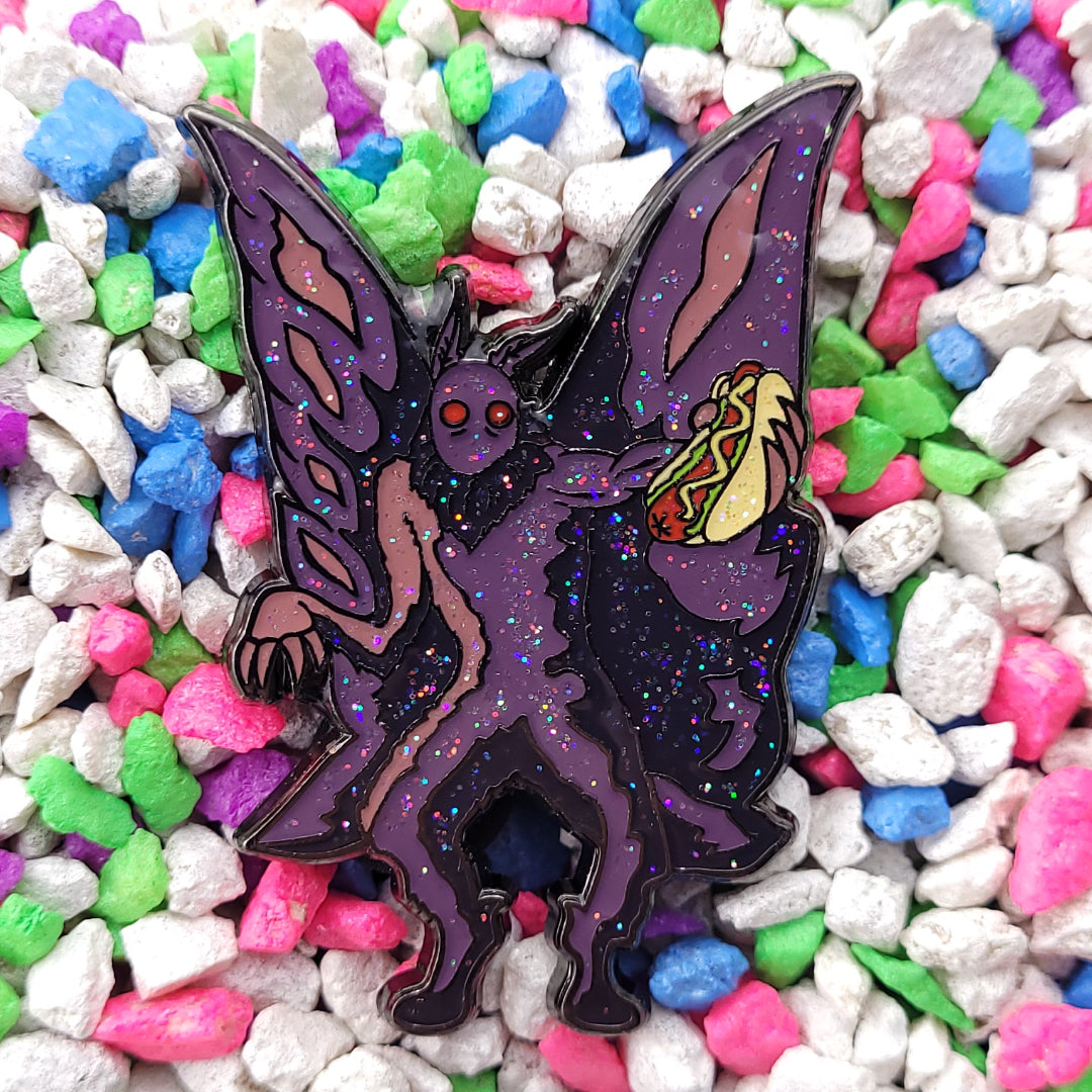An enamel pin of moth man holding a chicago style hotdog.