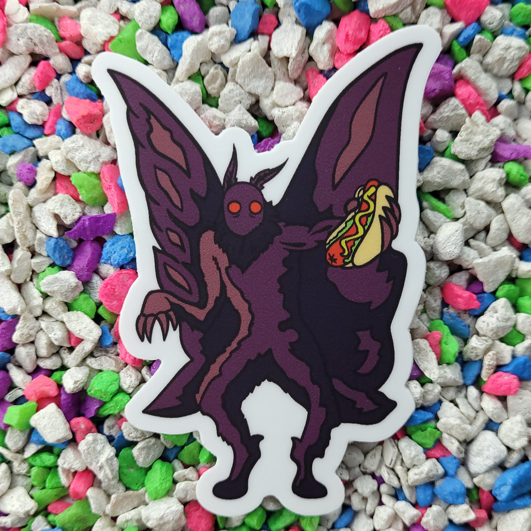 A sticker of a dark purple mothman holding a Chicago style hotdog in an outstretched hand.
