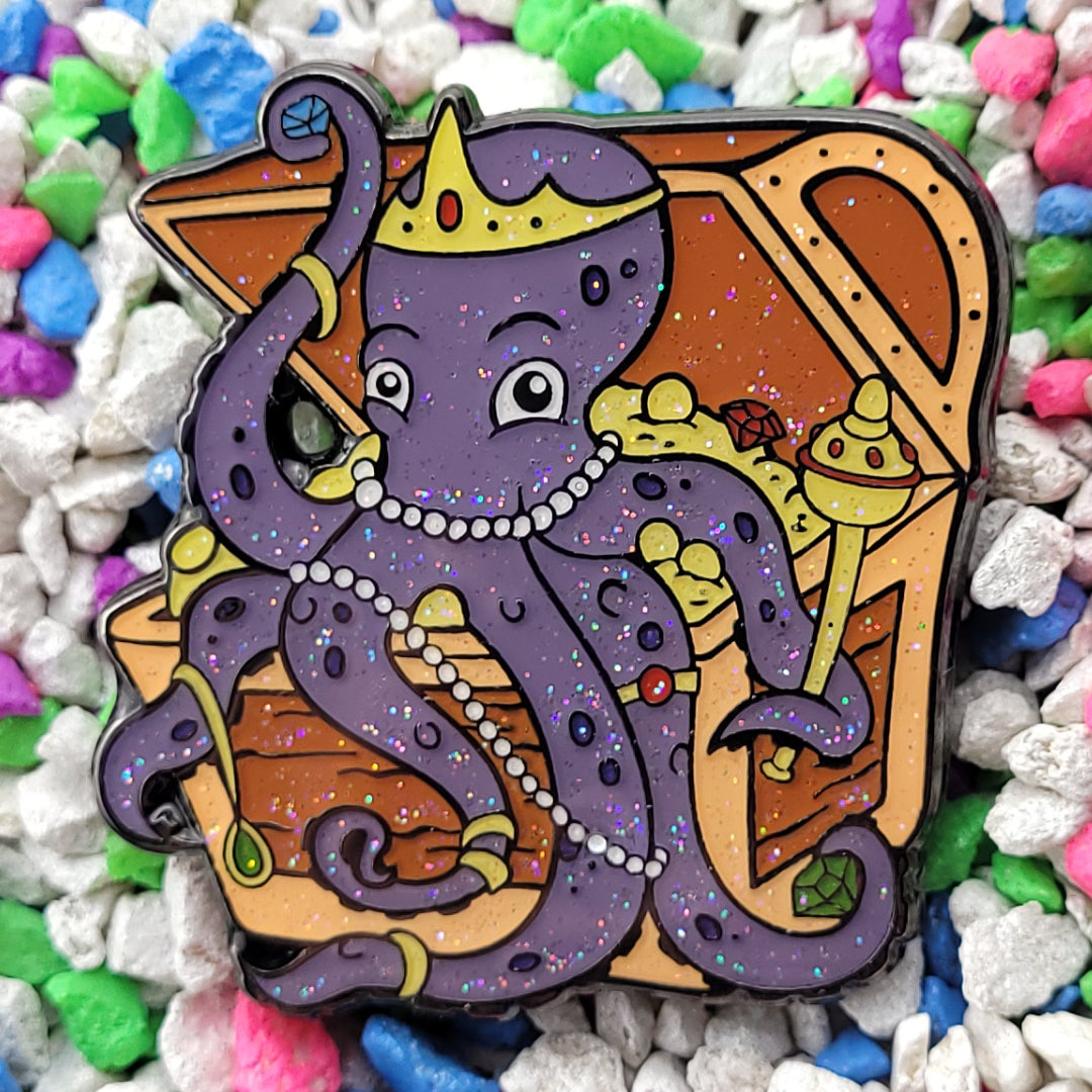 An enamel pin of an octopus sitting in a treasure chest adorning itself with gems, jewelry and accessories.