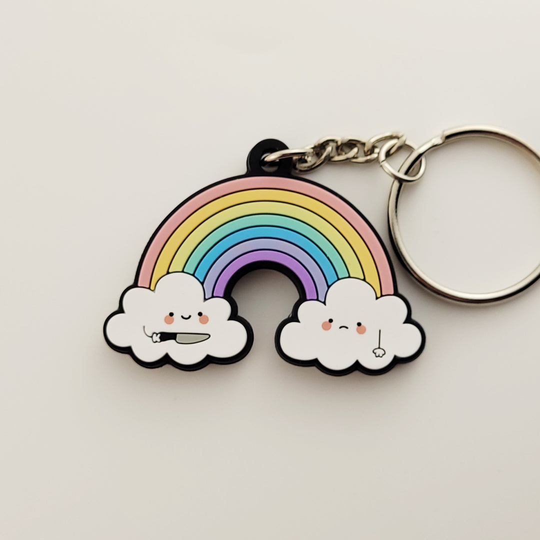 A rubber keychain with sturdy chain and ring featuring two kawaii cartoon clouds. One cloud is smiling and holding a knife, pointing it toward the other, who is frowning. This is a 2 sided keychain and the other side is mirrored.