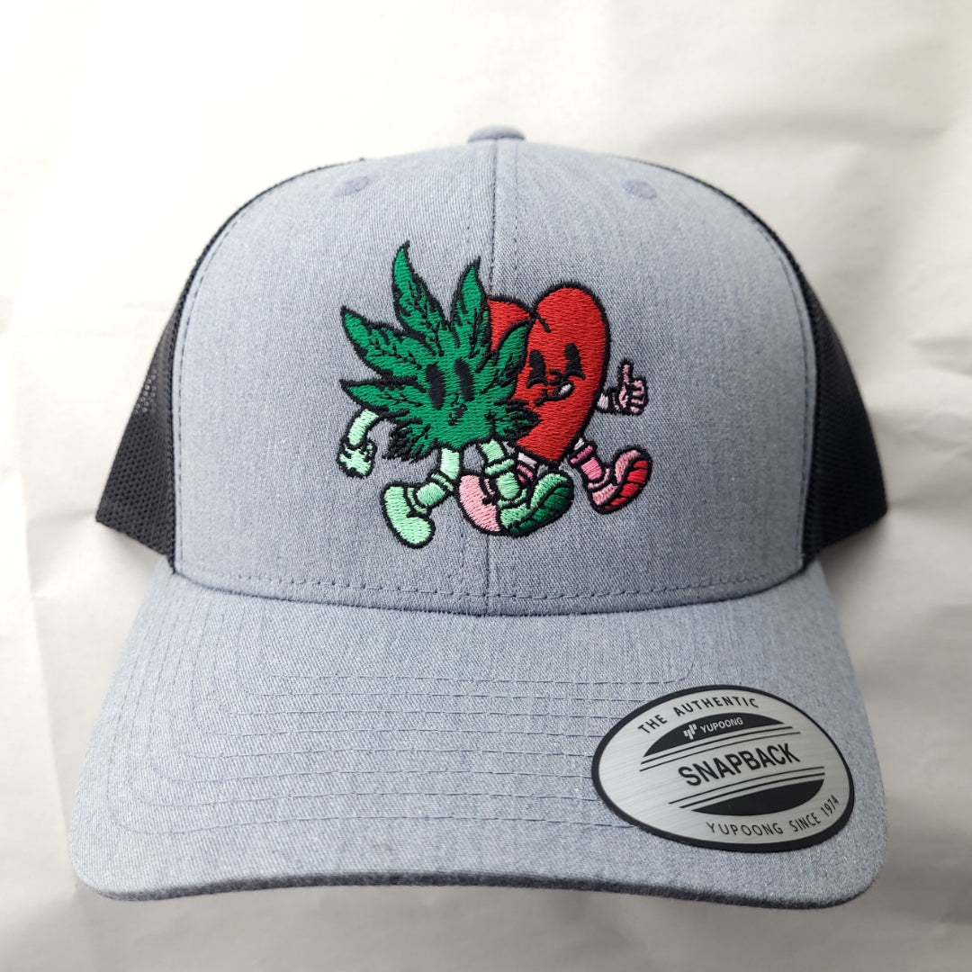 The front of a hat with an embroidered cartoon of a cannabis leaf and heart walking side by side. 